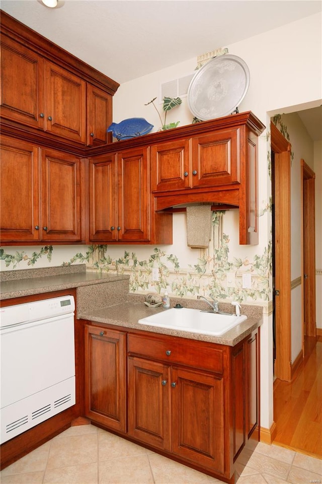 kitchen with dishwasher, light countertops, brown cabinetry, and a sink