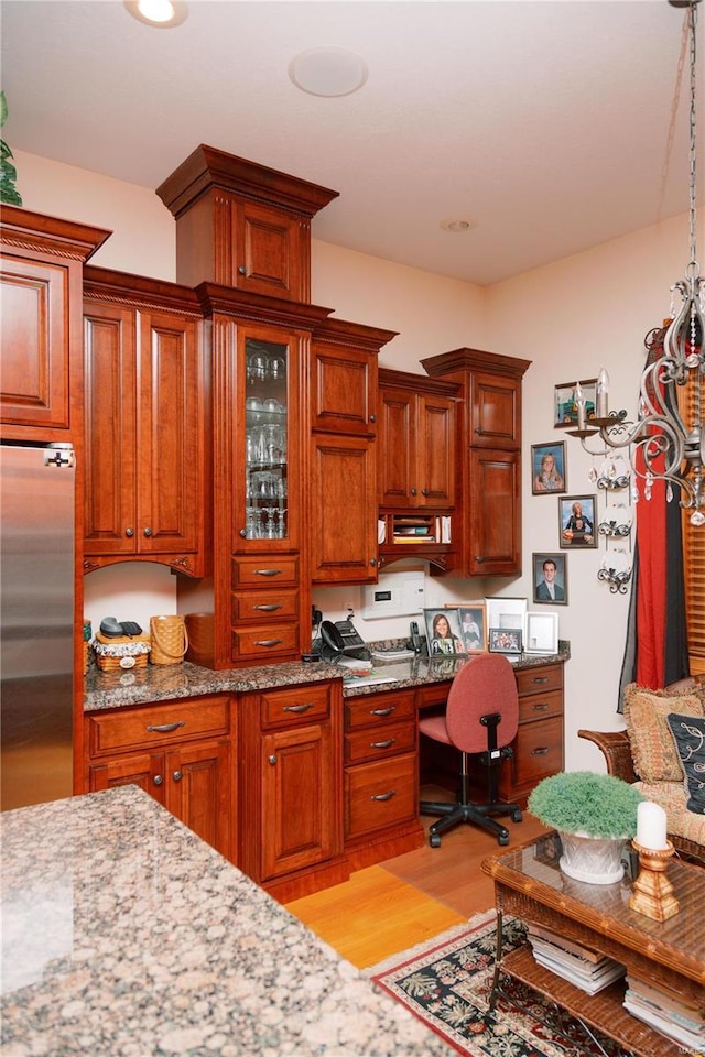 kitchen featuring light stone counters, brown cabinets, built in desk, light wood-style flooring, and stainless steel refrigerator