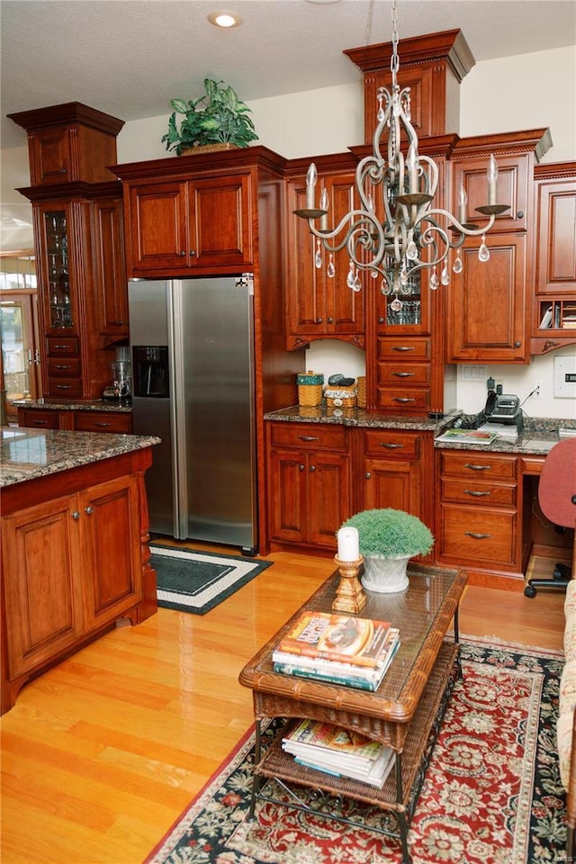 kitchen with dark stone counters, light wood finished floors, stainless steel refrigerator with ice dispenser, and a notable chandelier