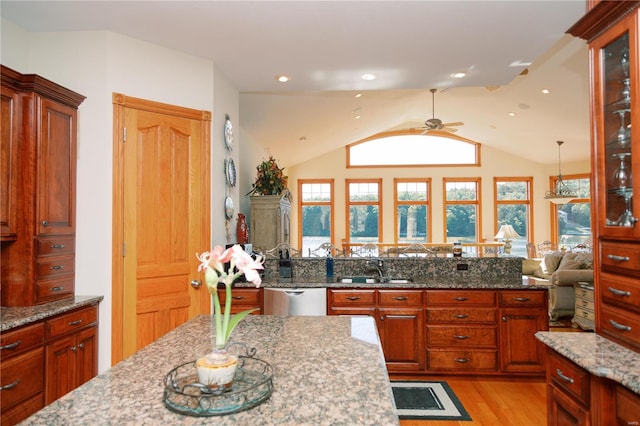 kitchen featuring light wood finished floors, lofted ceiling, light stone counters, a sink, and stainless steel dishwasher