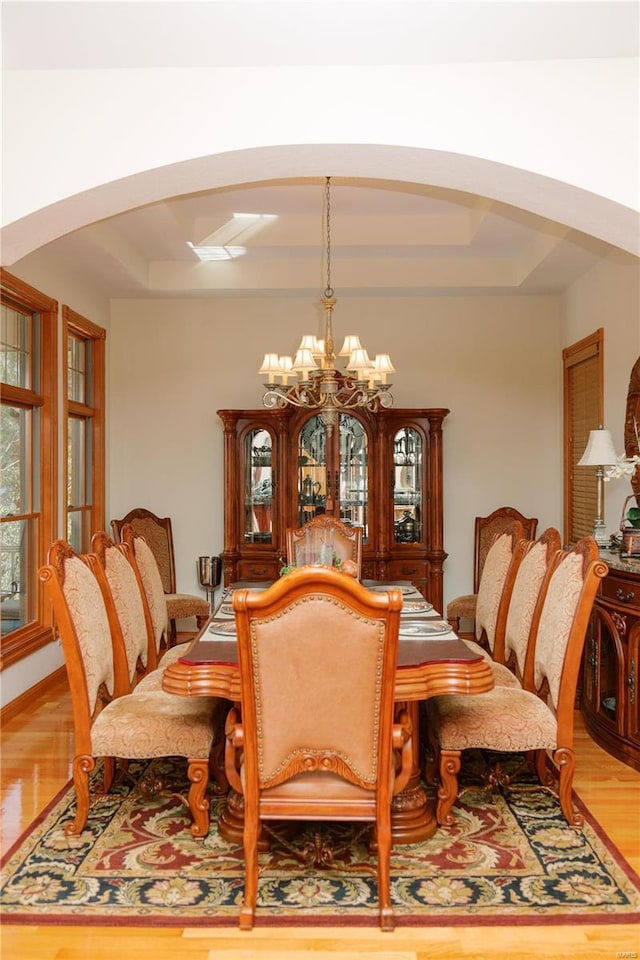 dining area with a chandelier, arched walkways, and a raised ceiling