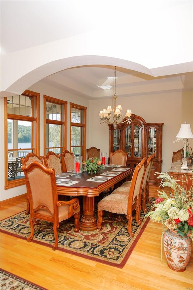 dining area with arched walkways, a chandelier, wood finished floors, and a raised ceiling