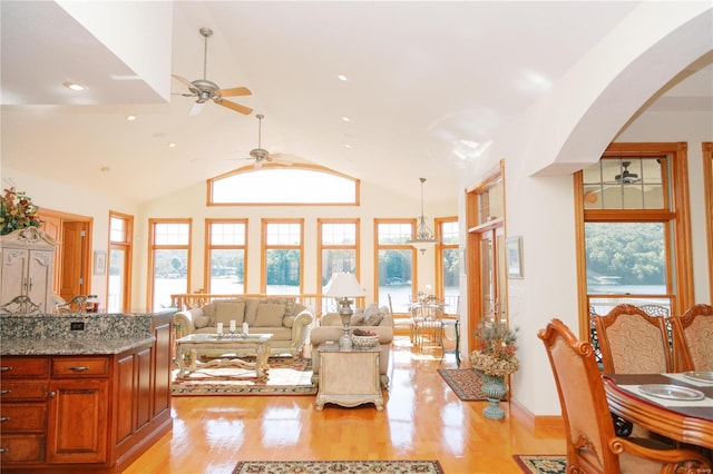 living room featuring arched walkways, high vaulted ceiling, plenty of natural light, and light wood-style flooring