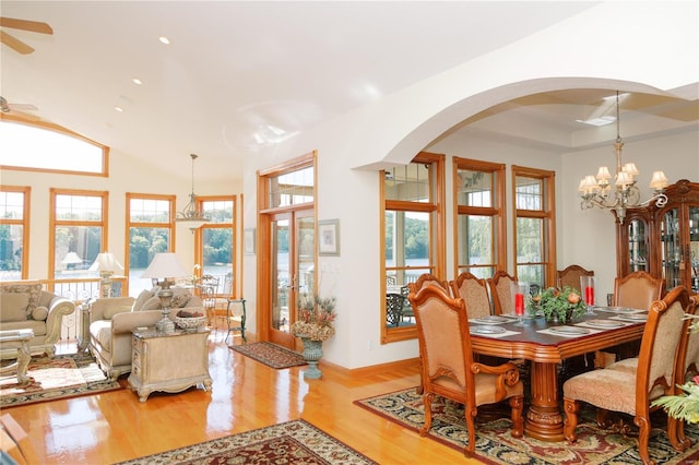 dining area with vaulted ceiling, a raised ceiling, ceiling fan with notable chandelier, and wood finished floors