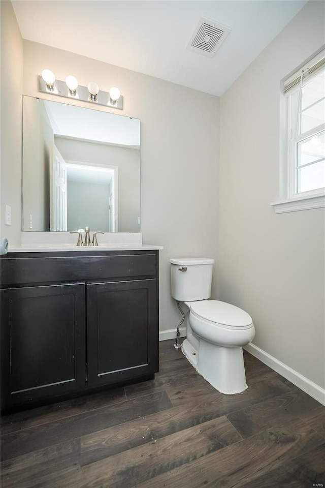 half bathroom featuring toilet, baseboards, visible vents, and wood finished floors