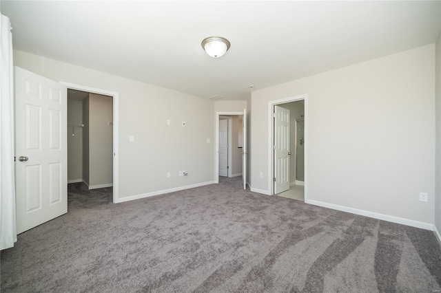 unfurnished bedroom featuring a spacious closet, a closet, carpet flooring, and baseboards