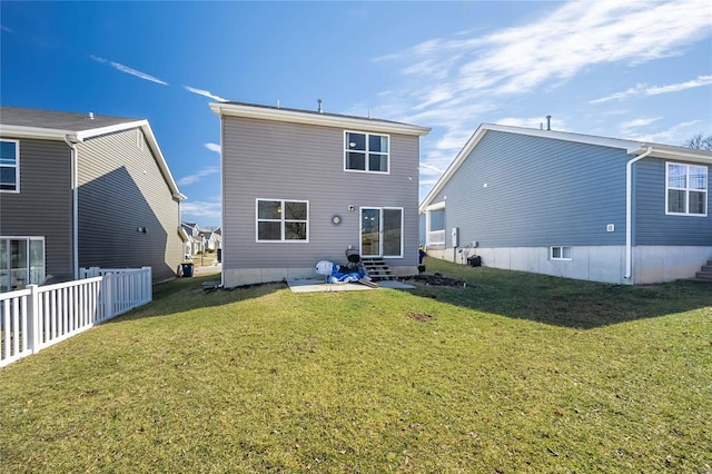 rear view of house featuring entry steps, a lawn, and fence