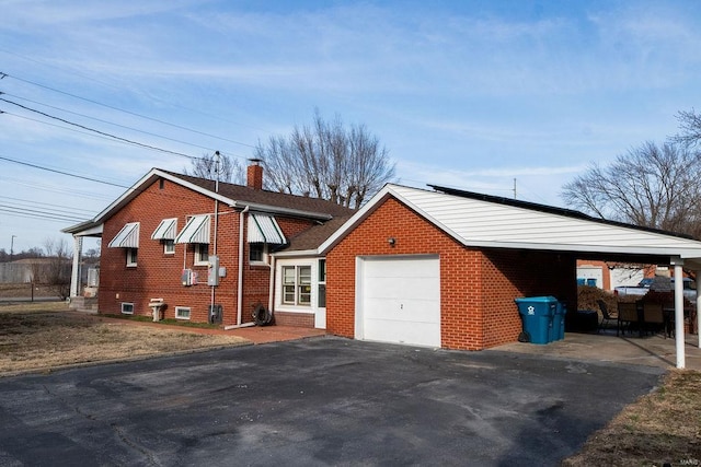 exterior space with brick siding, a chimney, a carport, a garage, and driveway