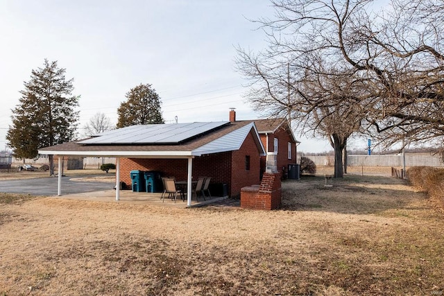 view of property exterior with brick siding, fence, roof mounted solar panels, a carport, and a chimney