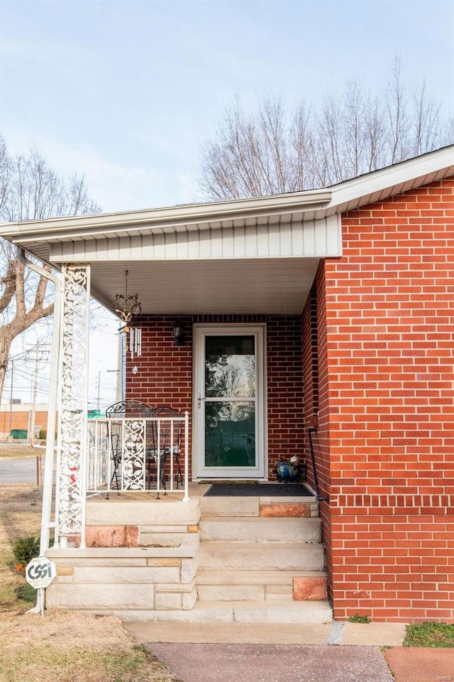 doorway to property with covered porch and brick siding