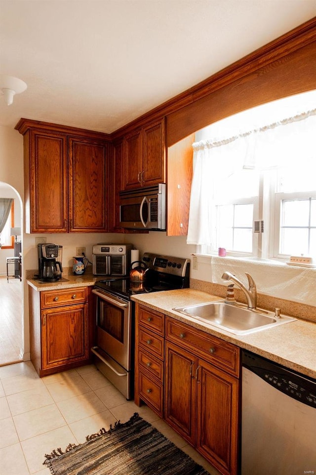 kitchen featuring arched walkways, light countertops, appliances with stainless steel finishes, and a sink