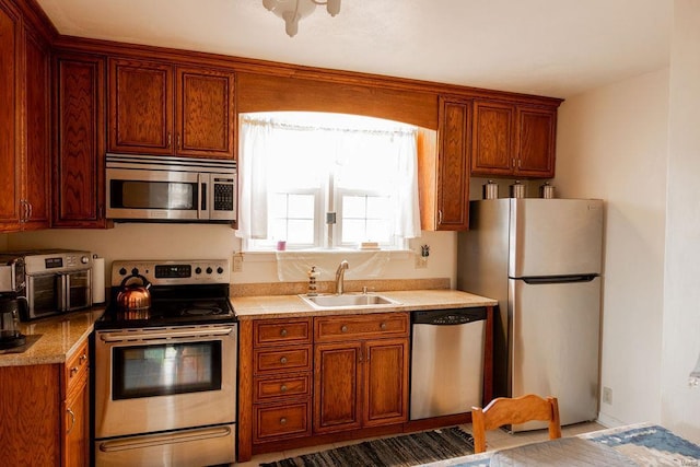 kitchen featuring light countertops, appliances with stainless steel finishes, brown cabinetry, and a sink