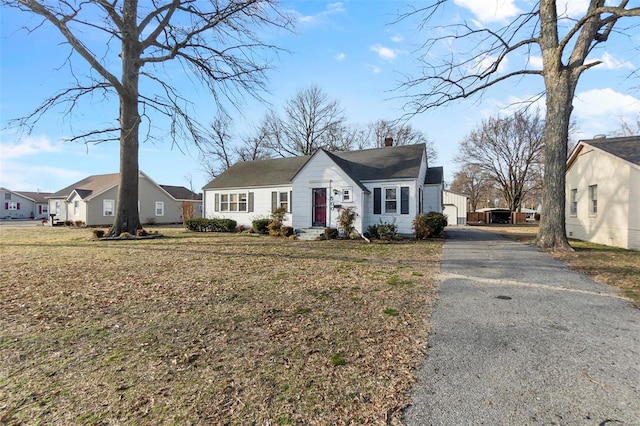 view of front facade with aphalt driveway, a chimney, a front yard, and a residential view