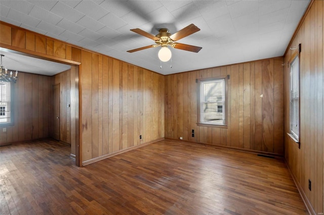 empty room with ceiling fan with notable chandelier, a healthy amount of sunlight, baseboards, and wood finished floors