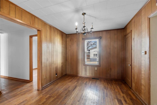 unfurnished dining area featuring a notable chandelier, visible vents, wooden walls, baseboards, and hardwood / wood-style flooring