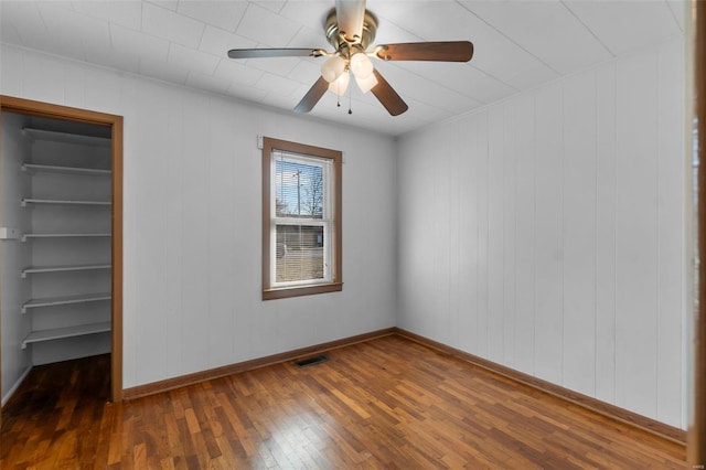 unfurnished bedroom featuring a walk in closet, a closet, visible vents, ceiling fan, and hardwood / wood-style floors