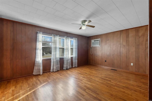 unfurnished room featuring wood walls, wood finished floors, visible vents, a ceiling fan, and baseboards