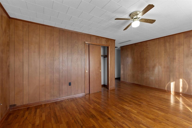 empty room with a ceiling fan, wooden walls, baseboards, and wood finished floors