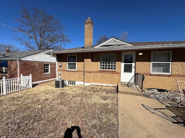 view of front of house with brick siding, a chimney, central AC, and fence