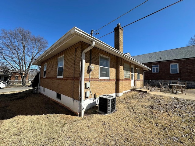 view of property exterior featuring a patio, central AC unit, brick siding, and a chimney