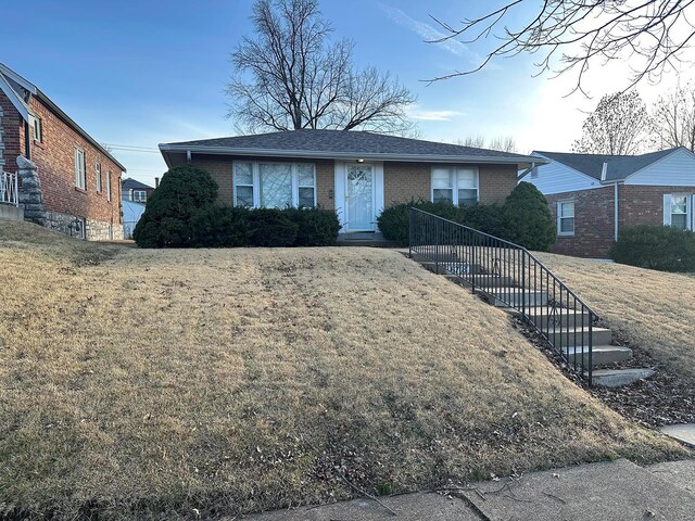 ranch-style house with brick siding, roof with shingles, and a front lawn