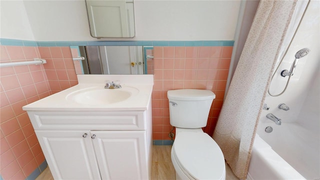 bathroom featuring toilet, vanity, wainscoting, shower / bathtub combination, and tile walls