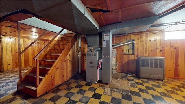 basement featuring tile patterned floors, wooden walls, stairway, and water heater