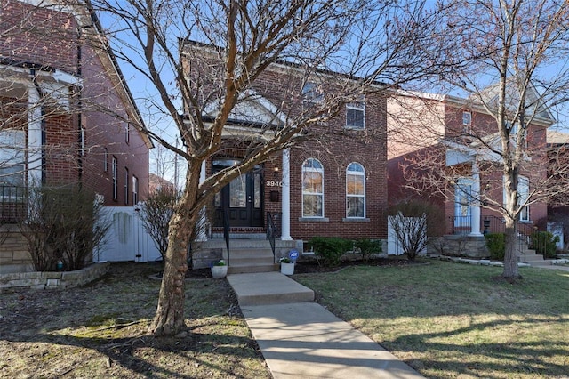 traditional-style home with a front yard, a gate, and brick siding