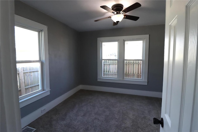 spare room with dark colored carpet, a ceiling fan, visible vents, and baseboards