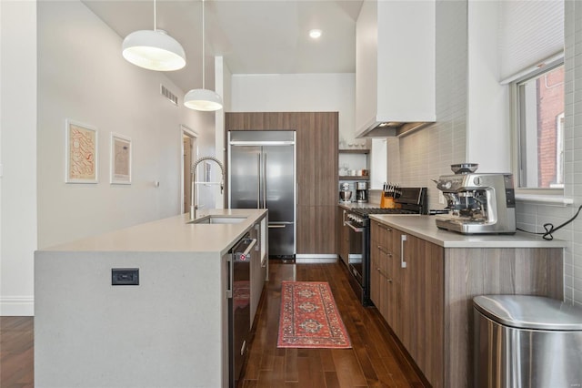 kitchen featuring a sink, light countertops, appliances with stainless steel finishes, tasteful backsplash, and dark wood finished floors