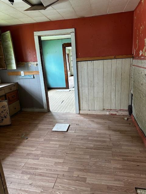 spare room with light wood-style floors, wainscoting, and a drop ceiling