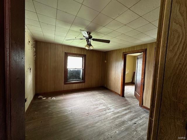 spare room featuring ceiling fan, wooden walls, baseboards, and wood finished floors