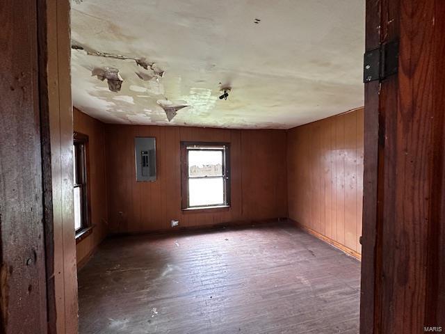 spare room with wooden walls, electric panel, baseboards, and wood finished floors