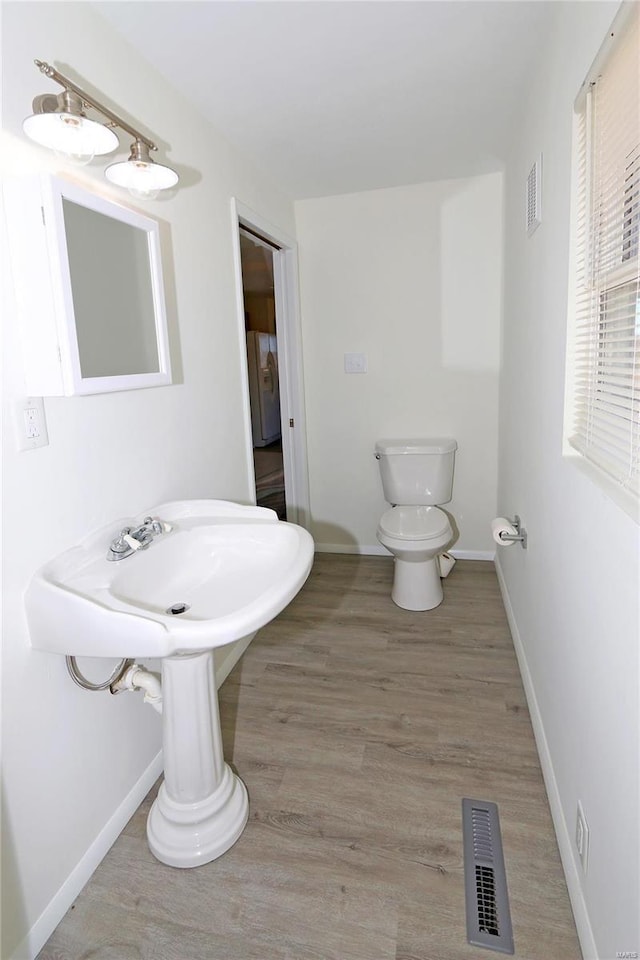 half bathroom with visible vents, toilet, baseboards, and wood finished floors