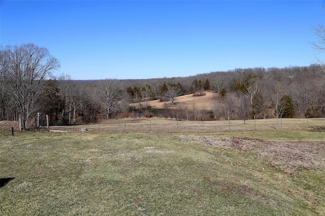 view of yard featuring a rural view, a wooded view, and fence