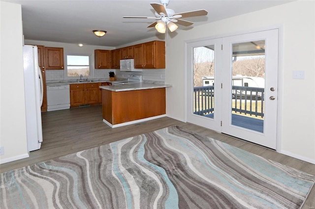 kitchen with a peninsula, white appliances, wood finished floors, brown cabinets, and tasteful backsplash