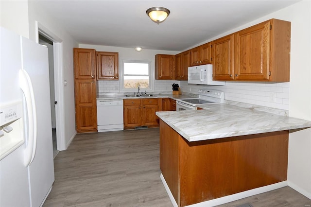 kitchen featuring white appliances, brown cabinetry, a peninsula, light countertops, and a sink