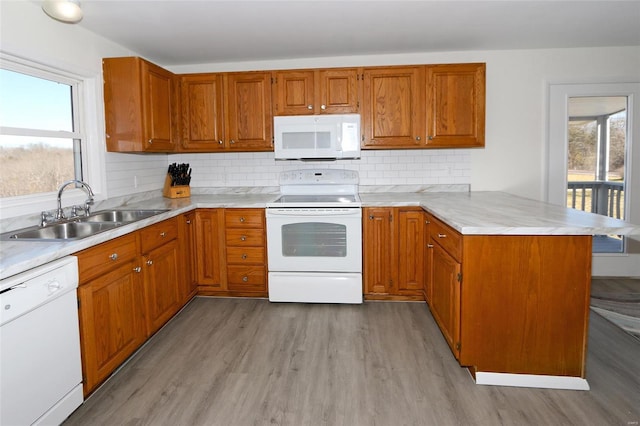 kitchen featuring white appliances, wood finished floors, a peninsula, light countertops, and a sink