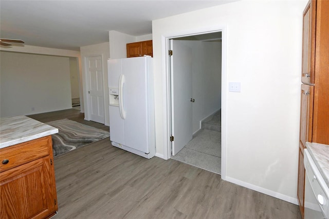 kitchen featuring baseboards, light countertops, brown cabinets, white fridge with ice dispenser, and light wood finished floors