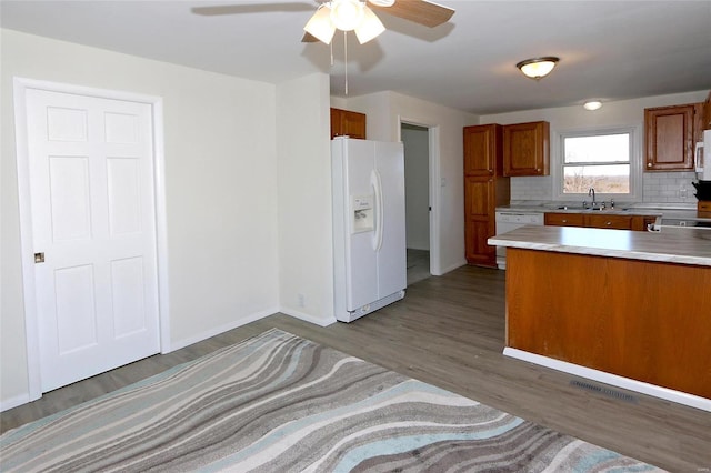 kitchen featuring white appliances, brown cabinets, wood finished floors, light countertops, and backsplash