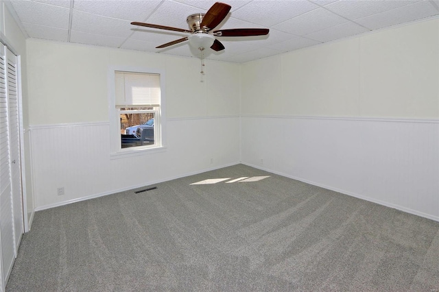 empty room featuring wainscoting, a drop ceiling, carpet, and visible vents