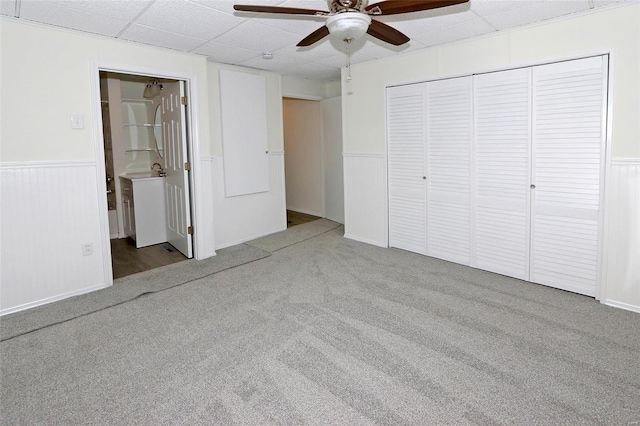 unfurnished bedroom featuring a paneled ceiling, a closet, a wainscoted wall, and carpet flooring