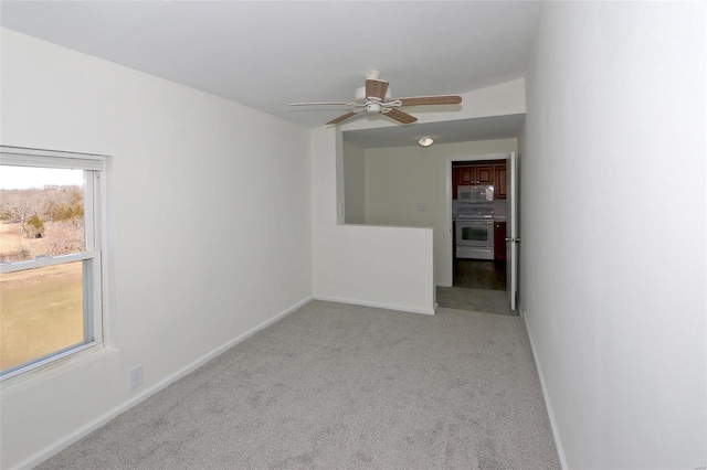 carpeted spare room featuring baseboards and a ceiling fan