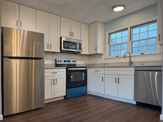 kitchen with appliances with stainless steel finishes, stone countertops, a sink, and white cabinets