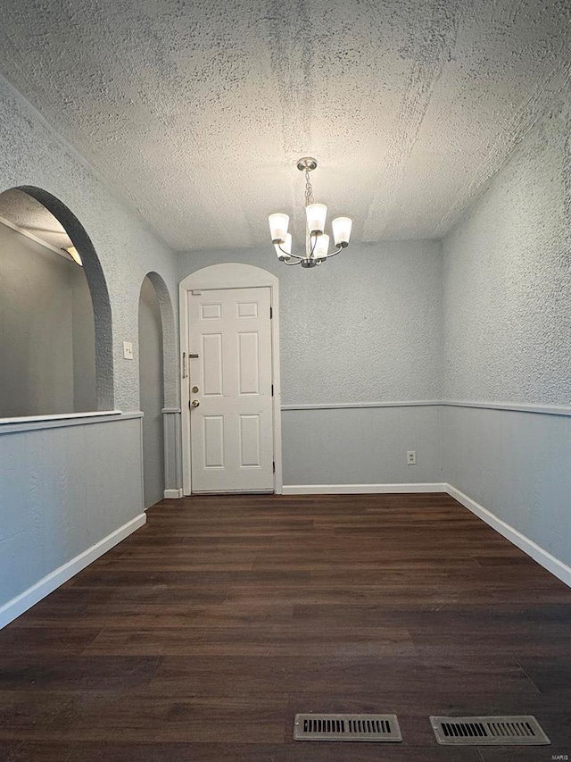 unfurnished dining area with wood finished floors, visible vents, a textured wall, and an inviting chandelier