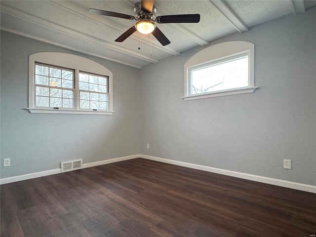 spare room featuring a textured ceiling, wood finished floors, visible vents, baseboards, and beamed ceiling