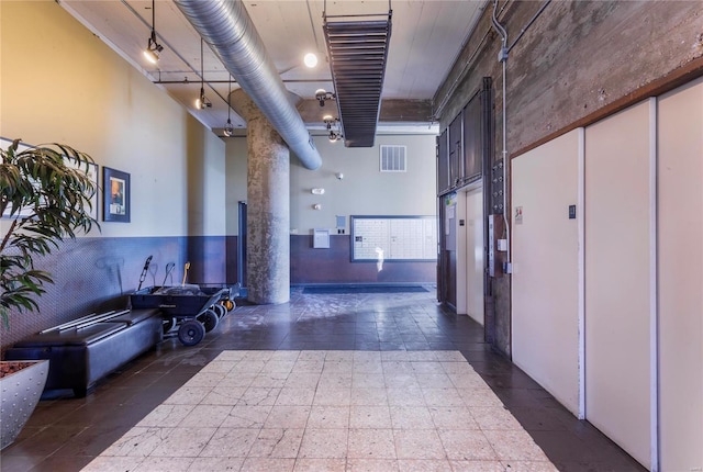 interior space featuring elevator, a high ceiling, visible vents, and track lighting