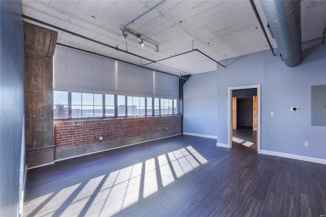 spare room with brick wall, wood finished floors, baseboards, electric panel, and rail lighting