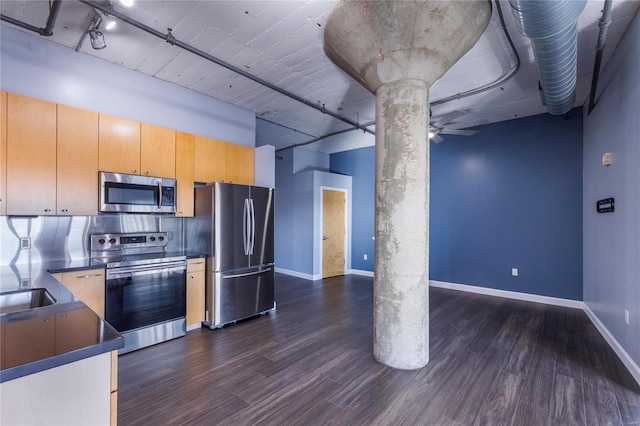 kitchen with dark countertops, appliances with stainless steel finishes, dark wood-type flooring, track lighting, and baseboards