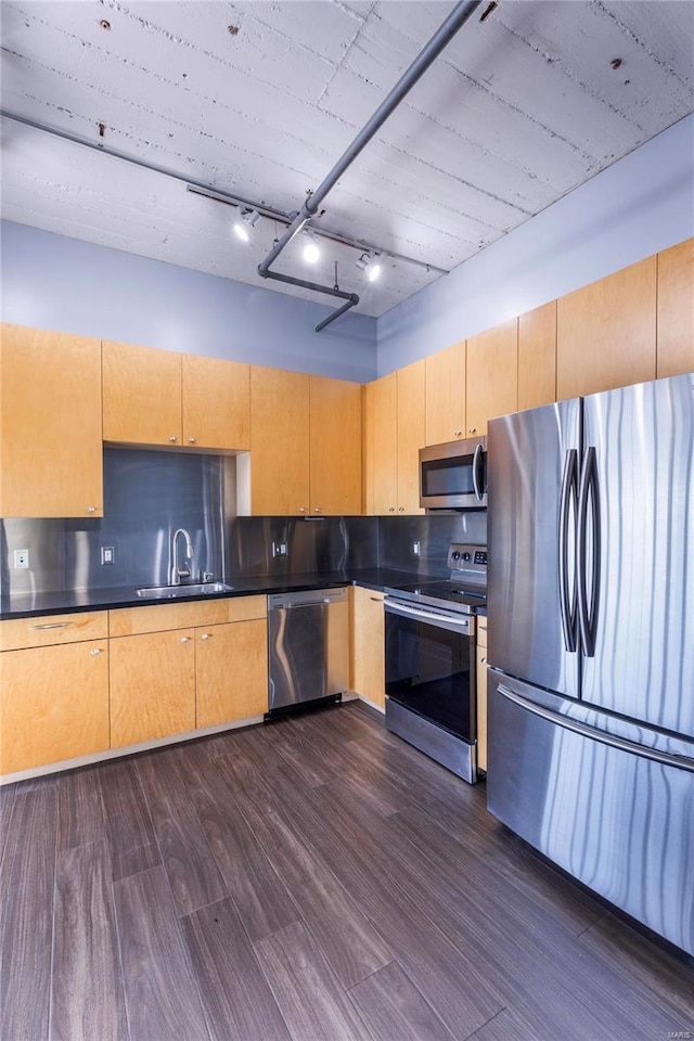 kitchen with dark wood-style floors, stainless steel appliances, dark countertops, decorative backsplash, and a sink